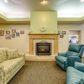 A cozy living room featuring a fireplace, floral-patterned couch, and armchair with family photos adorning the walls.
