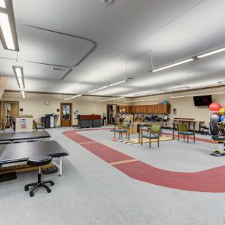 A spacious activity room designed for therapeutic purposes, featuring several tables, chairs, and equipment.