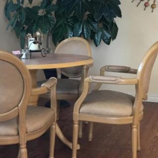A cozy dining area with a round table and four upholstered chairs, surrounded by indoor plants.