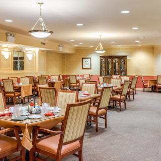 An empty dining room with neatly arranged tables and chairs, warmly lit by ceiling lights.