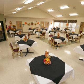 An indoor dining area with tables and chairs arranged, each table adorned with black tablecloths and fall-themed decorations.