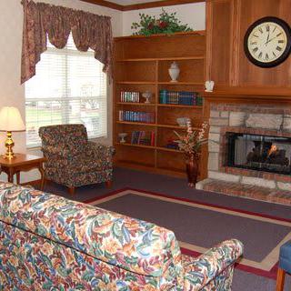 A cozy living room with a colorful sofa, armchair, bookshelf, and a fireplace beneath a clock.