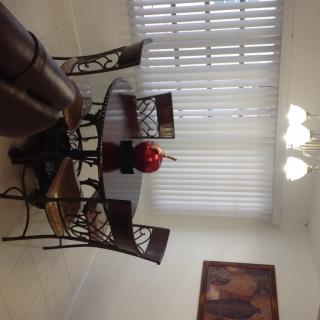 A dining room with a round glass table, ornate chairs, a chandelier, and window blinds.