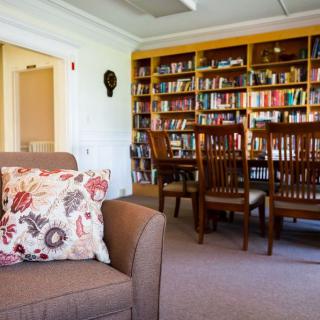 A cozy library space featuring bookshelves, a comfortable couch with floral cushions, and a wooden table set with chairs.
