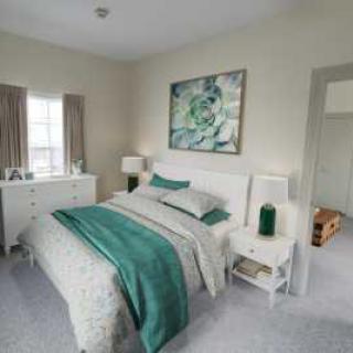 A modern bedroom featuring a bed with green accent blankets and pillows, complemented by artwork on the wall and light-colored furniture.