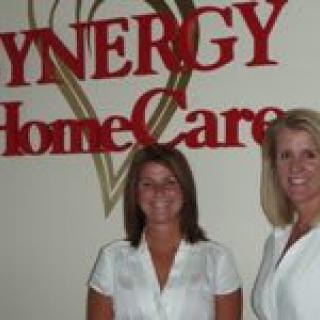 Two individuals standing in front of Synergy HomeCare signage.