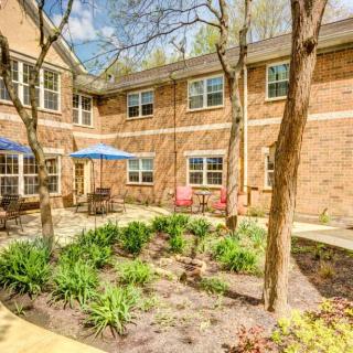 A charming courtyard with lush greenery and comfortable outdoor seating in front of a brick building.
