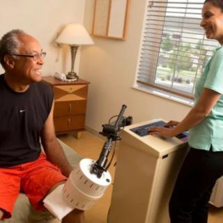 A patient sitting with a physical therapist during a rehabilitation session involving medical equipment.