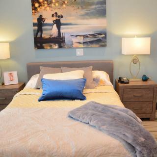 A cozy and modern bedroom with a neatly made bed, stylish artwork above the headboard, and warm lighting from two matching lamps on either side.
