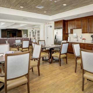 A modern dining area with several tables and chairs, featuring a hardwood floor and an adjoining kitchen space.