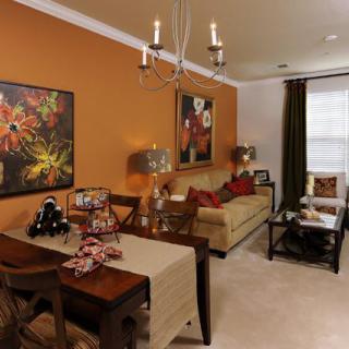 A cozy living room with an orange accent wall, featuring a dining area and colorful artwork.