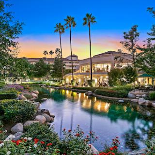 A picturesque resort landscape at sunset, featuring palm trees and a serene water reflection.