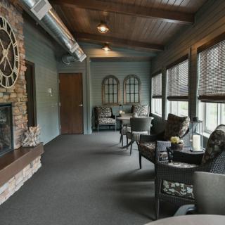 A cozy indoor seating area featuring a brick fireplace and large decorative clock, with comfortable furniture and ample windows.