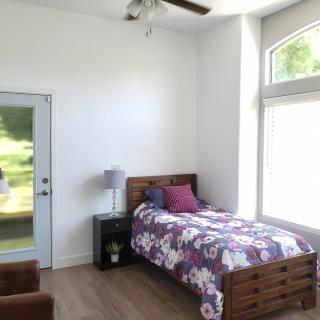 A minimalist bedroom featuring a single bed with floral bedding, large windows, and ample natural light.