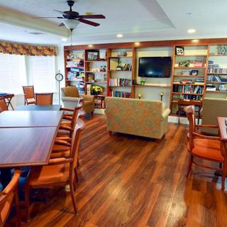 A cozy living room with wooden floors, featuring bookshelves, a television, and ample seating with tables and chairs.