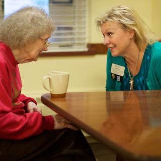 A caregiver and an elderly person engaged in a friendly conversation at a care facility.