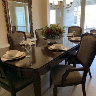 A stylish dining room featuring a dark wood table set with elegant chairs, complemented by a large mirror and chandelier.