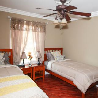 A cozy bedroom with twin beds, featuring wooden furniture and a ceiling fan.