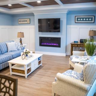 A cozy living room with blue walls, featuring a striped sofa, television, and modern fireplace.