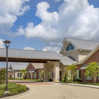 A modern building with a covered entrance and landscaped surroundings under a cloudy sky.