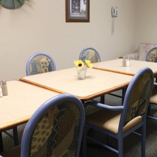 A cozy dining room with a rectangular table, surrounded by chairs and adorned with flowers in a vase.