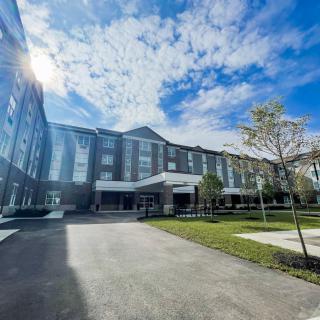 A modern building under a partly cloudy sky, surrounded by trees.