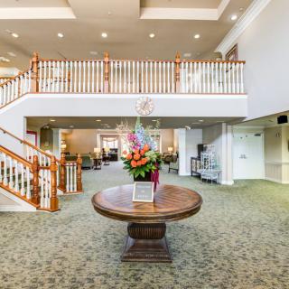 A spacious lobby with elegant interior design featuring a central table adorned with a flower arrangement, and a staircase leading to the upper level.