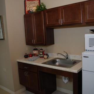 A small kitchen area with a sink, upper and lower cabinets, a microwave, and a refrigerator.