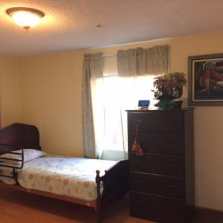 A simple bedroom with a single bed, a dresser, and a window with curtains.