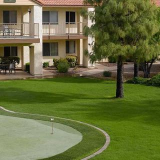 A view of a hotel with a putting green surrounded by lush greenery and trees.
