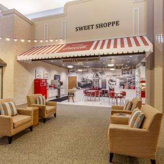 A cozy interior featuring a vintage-style sweet shop with a red and white striped awning, alongside a comfortable seating area.