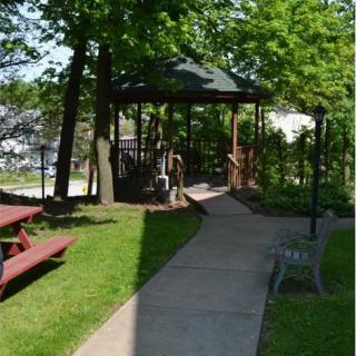 A serene park scene featuring a pathway leading to a gazebo surrounded by trees, with a picnic table and bench nearby.