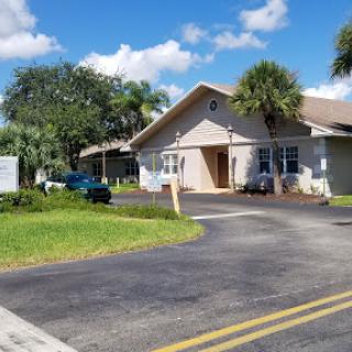 A charming residential house surrounded by greenery and palm trees under a bright blue sky.