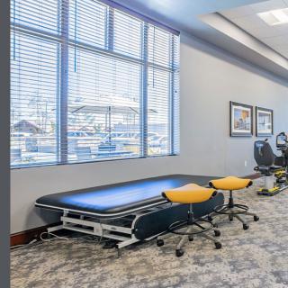 A physical therapy clinic with a treatment table, chairs, and exercise equipment.