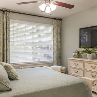 A cozy bedroom with a large window, neatly made bed, and a dresser with decorative items.