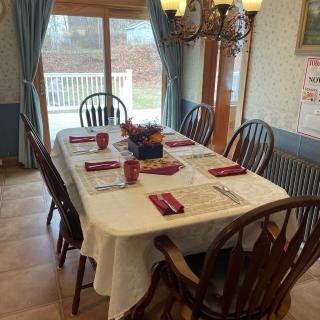 A dining room table set for a meal, featuring six chairs and neatly arranged place settings under a chandelier.
