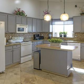 A modern kitchen with gray cabinets and a central island, featuring pendant lights and tiled flooring.