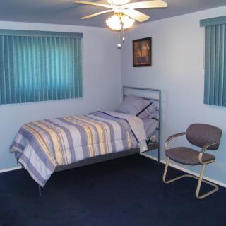 A simple bedroom with a single bed, ceiling fan, and chair.