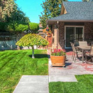 A serene backyard featuring a well-maintained lawn, patio with outdoor dining furniture, and lush plants.