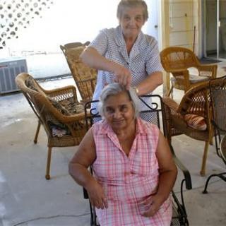 Two elderly women enjoying a haircut outside on the patio.