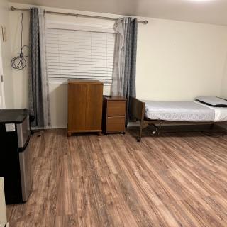 A minimalist room with wooden flooring, featuring a single bed, a small dresser, and a chest of drawers.
