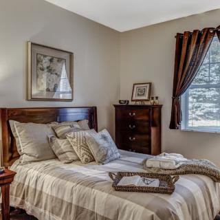 A cozy bedroom with a neatly made bed, decorative pillows, and a wooden dresser by the window.
