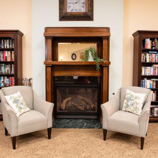 A cozy living room with armchairs and a fireplace, flanked by bookshelves.