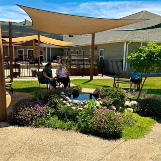A peaceful garden setting with a shaded seating area and vibrant greenery.