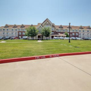 A large hotel building with a well-maintained lawn and parking area in the foreground.