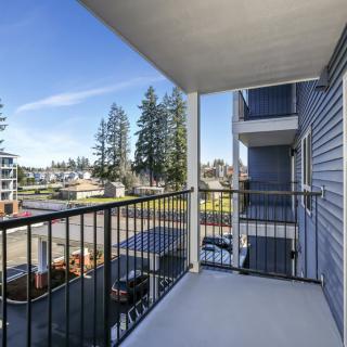 A spacious balcony with a view of neighboring buildings and tall trees under a clear blue sky.