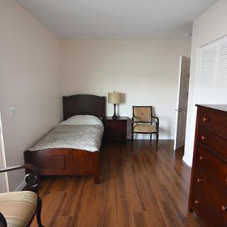 A minimalist bedroom featuring a single bed with wooden furniture and a hardwood floor.