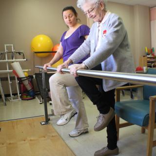 An elderly person participates in a physical therapy session with the assistance of a caregiver.