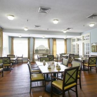 A spacious dining room with multiple tables and chairs, featuring large windows and wooden flooring.