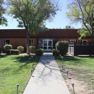 A building with a concrete pathway leading to its entrance, surrounded by trees and grass.